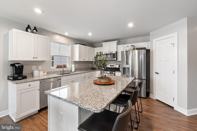 kitchen featuring dark wood-style flooring, appliances with stainless steel finishes, white cabinets, a sink, and a kitchen breakfast bar