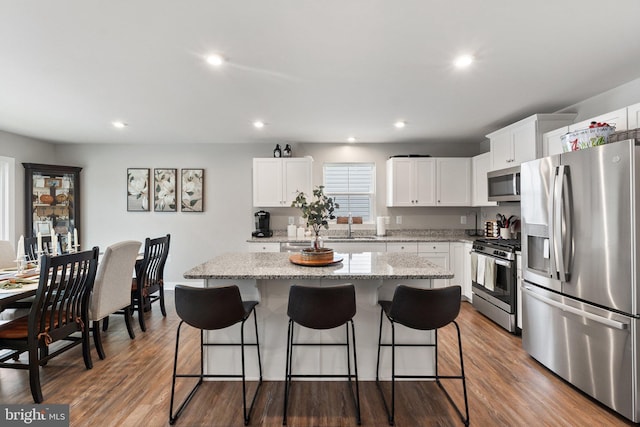 kitchen featuring dark wood-style floors, a kitchen island, a kitchen bar, and appliances with stainless steel finishes