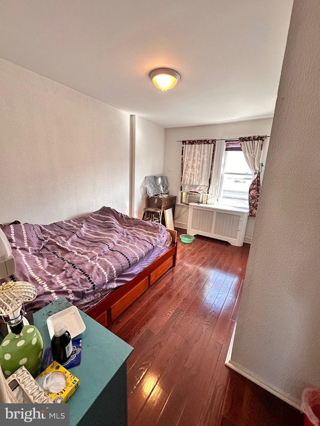 bedroom featuring radiator heating unit, dark wood finished floors, and a textured wall