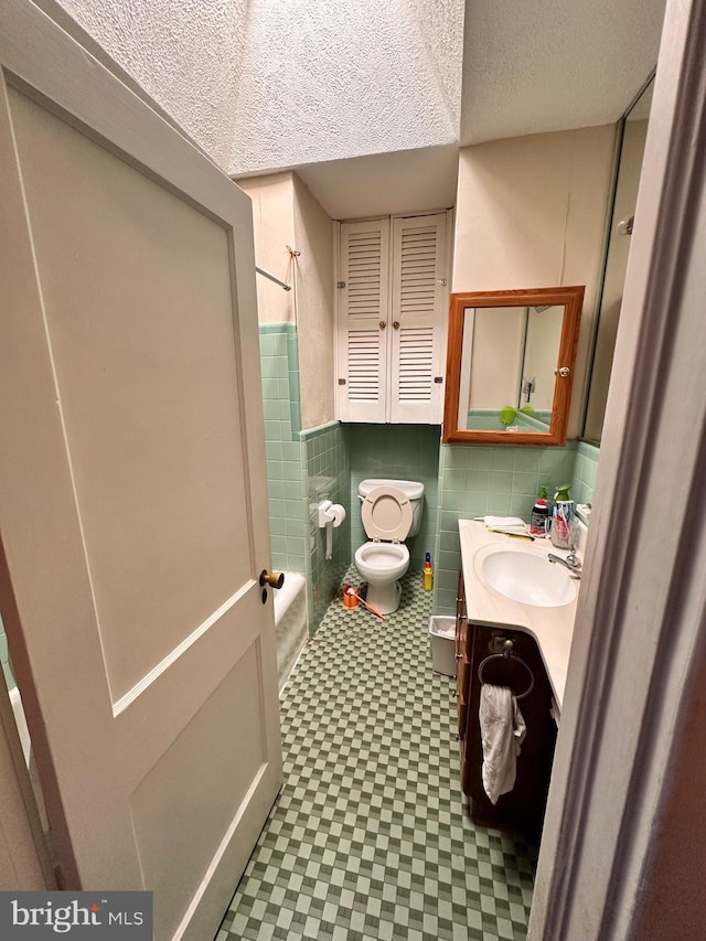 full bath with tile walls, toilet, a textured ceiling, shower / tub combination, and vanity