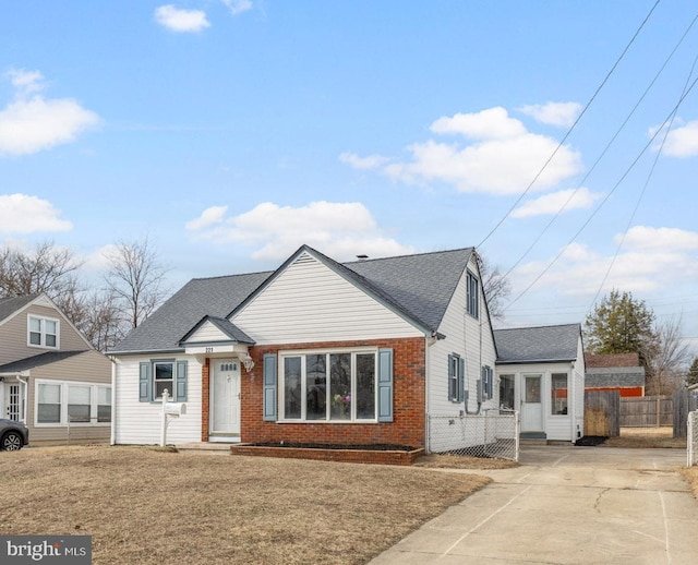 view of front facade featuring a shingled roof, brick siding, fence, and a front lawn