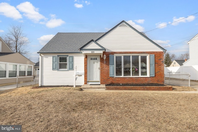 bungalow featuring roof with shingles, a front yard, fence, and brick siding