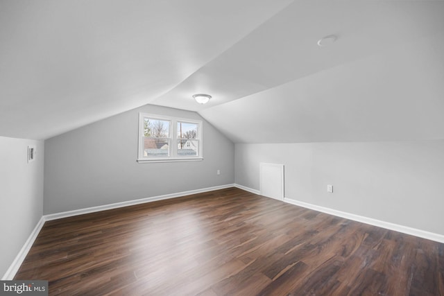 additional living space with dark wood-style flooring, visible vents, vaulted ceiling, and baseboards