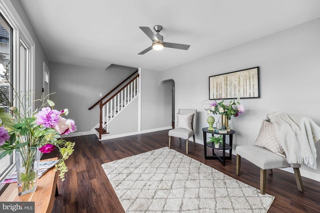 living area featuring arched walkways, dark wood-type flooring, stairway, and baseboards