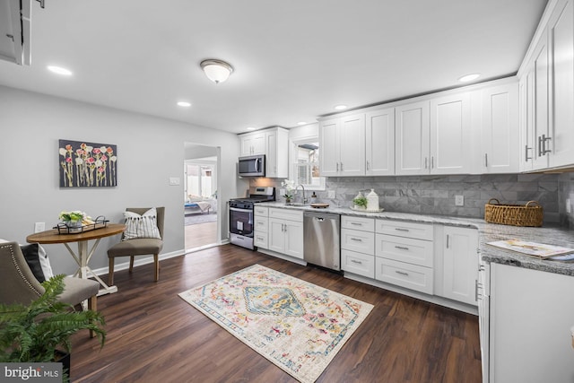 kitchen with dark wood-style floors, appliances with stainless steel finishes, white cabinets, and light stone counters