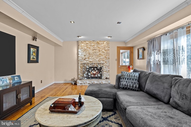 living room with baseboards, a stone fireplace, light wood finished floors, and crown molding