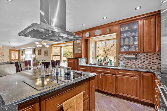 kitchen with black electric cooktop, island range hood, a sink, dark stone counters, and glass insert cabinets