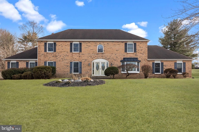 colonial-style house featuring brick siding, a front lawn, and roof with shingles