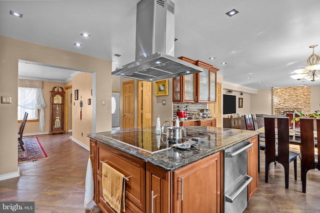 kitchen featuring island exhaust hood, brown cabinetry, glass insert cabinets, a kitchen island, and dark stone countertops