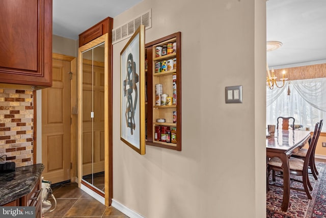 hallway with dark tile patterned floors and a notable chandelier