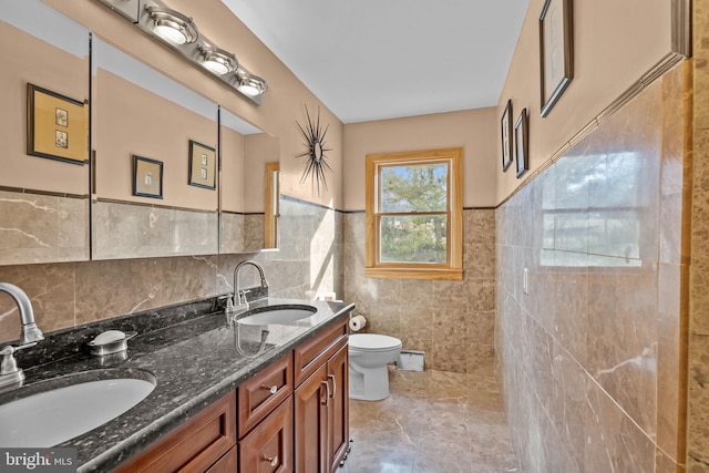 full bath featuring double vanity, a sink, toilet, and tile walls