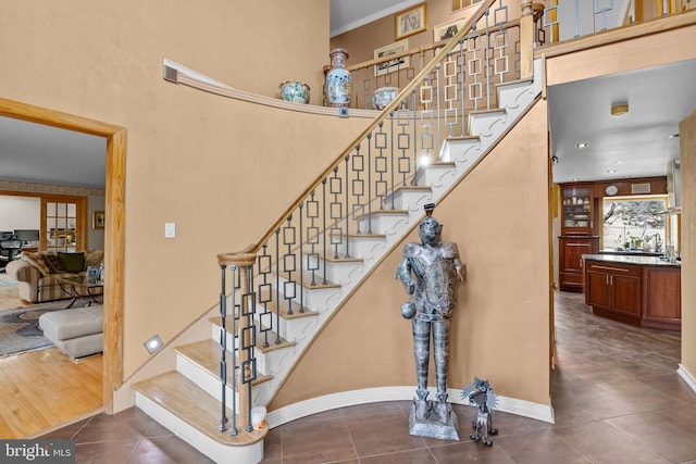 stairway featuring baseboards, ornamental molding, a towering ceiling, and tile patterned floors