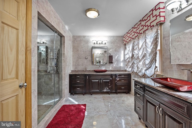 full bath featuring a sink, a shower stall, two vanities, and tile walls