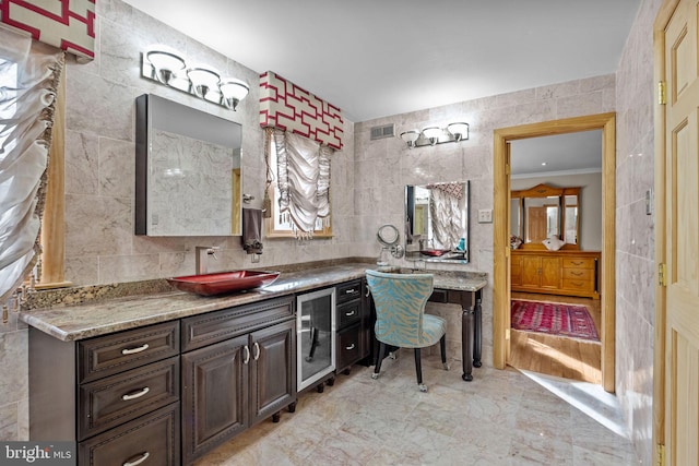 bathroom featuring beverage cooler, visible vents, ornamental molding, vanity, and tile walls