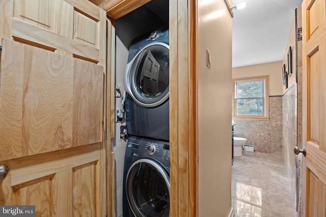 laundry room featuring laundry area, tile walls, stacked washer / drying machine, and a wainscoted wall