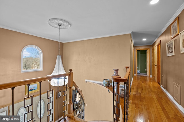 corridor featuring visible vents, baseboards, an upstairs landing, light wood-type flooring, and crown molding