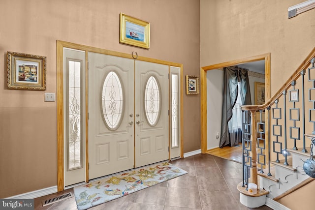 foyer featuring stairs, visible vents, a towering ceiling, baseboards, and tile patterned floors