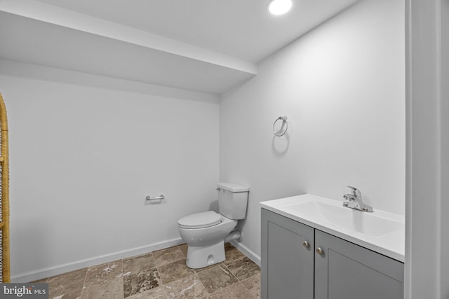 half bath featuring stone finish floor, baseboards, vanity, and toilet