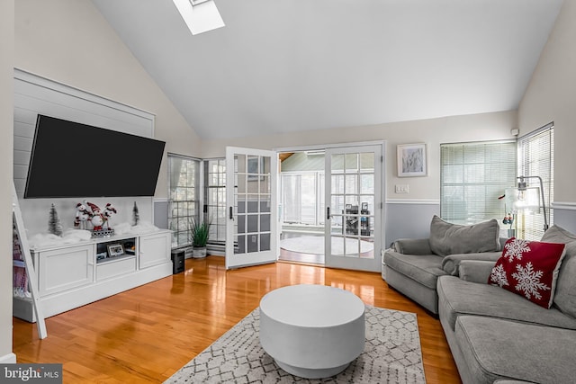 living area featuring high vaulted ceiling, a skylight, french doors, and light wood finished floors