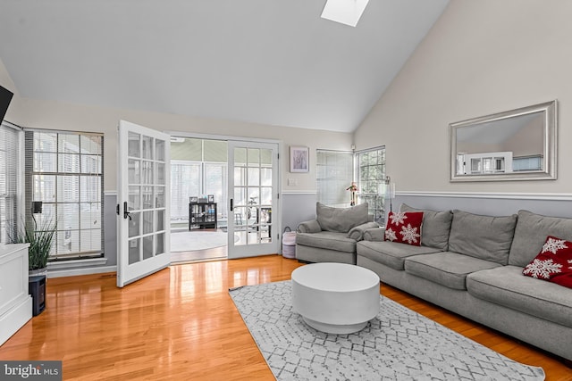 living room featuring a skylight, high vaulted ceiling, and light wood finished floors