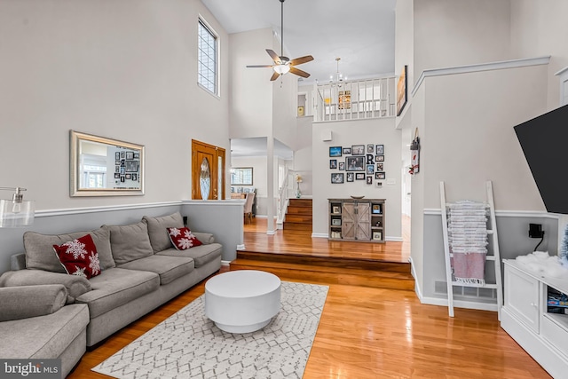 living area with baseboards, a ceiling fan, stairway, a high ceiling, and light wood-type flooring