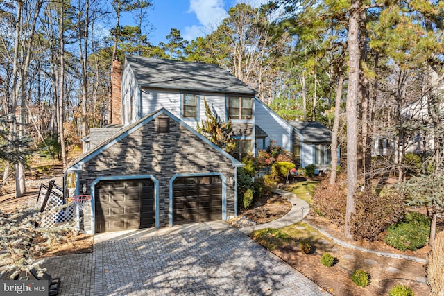 exterior space featuring an attached garage, a chimney, and decorative driveway