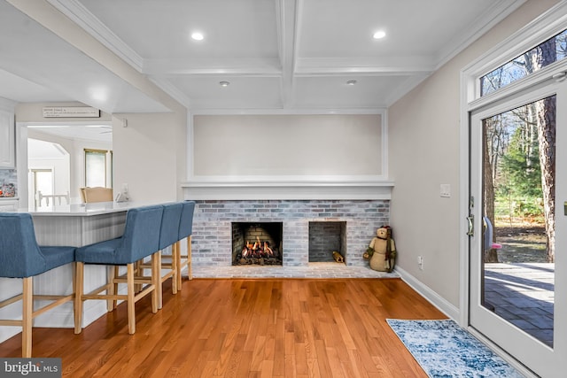 living area featuring light wood finished floors, a fireplace, beam ceiling, and crown molding