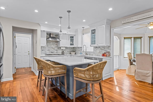 kitchen with a kitchen breakfast bar, light countertops, wall chimney range hood, white cabinetry, and a sink