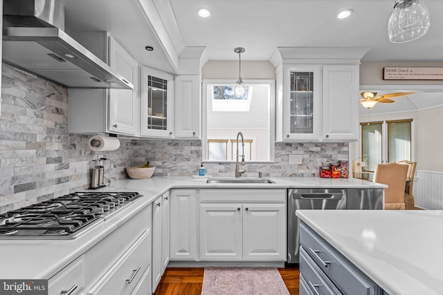 kitchen with decorative light fixtures, stainless steel appliances, white cabinetry, a sink, and wall chimney exhaust hood