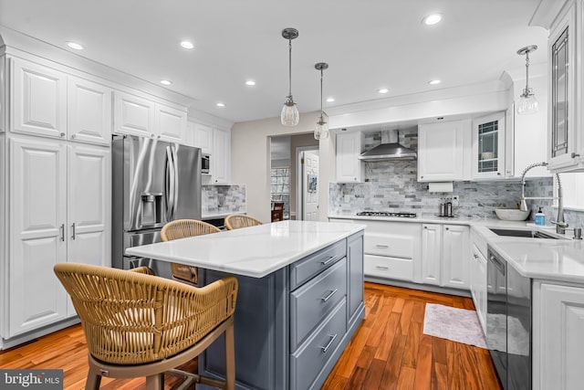 kitchen with stainless steel appliances, a sink, white cabinets, gray cabinets, and wall chimney exhaust hood