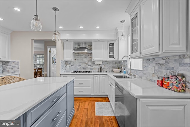 kitchen featuring light countertops, wall chimney range hood, a sink, and white cabinets