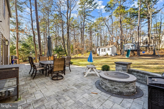 view of patio / terrace with an outdoor fire pit, outdoor dining area, a playground, an outdoor structure, and grilling area