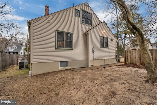 back of property with a fenced backyard, a chimney, and central AC