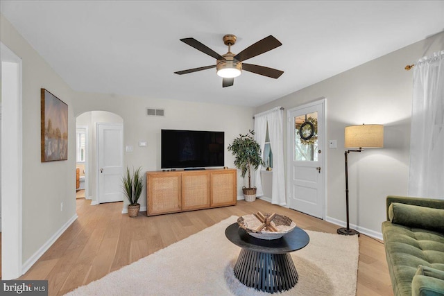 living area featuring arched walkways, ceiling fan, visible vents, and light wood-style floors