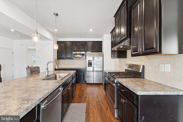 kitchen with a sink, appliances with stainless steel finishes, hanging light fixtures, under cabinet range hood, and dark wood-style flooring