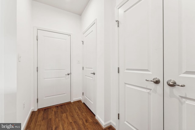 corridor featuring baseboards and dark wood-type flooring