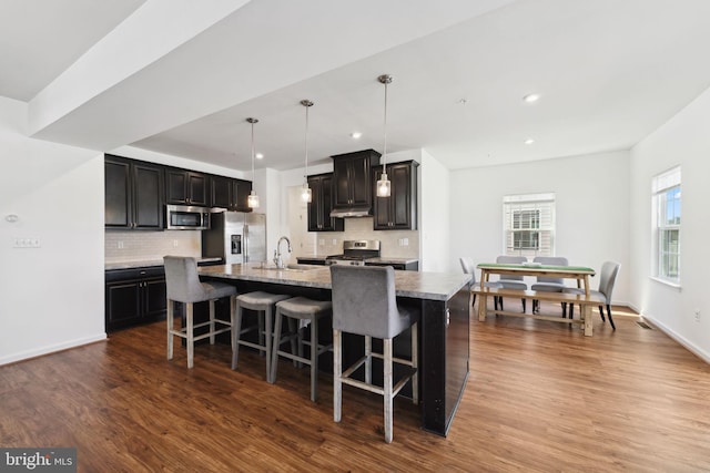 kitchen with a large island with sink, a kitchen bar, dark wood finished floors, a sink, and appliances with stainless steel finishes