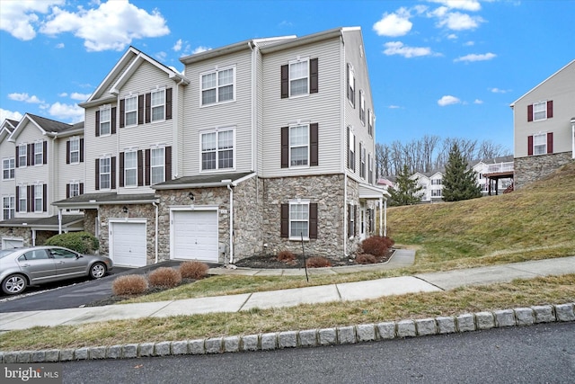 multi unit property featuring driveway, stone siding, and a garage