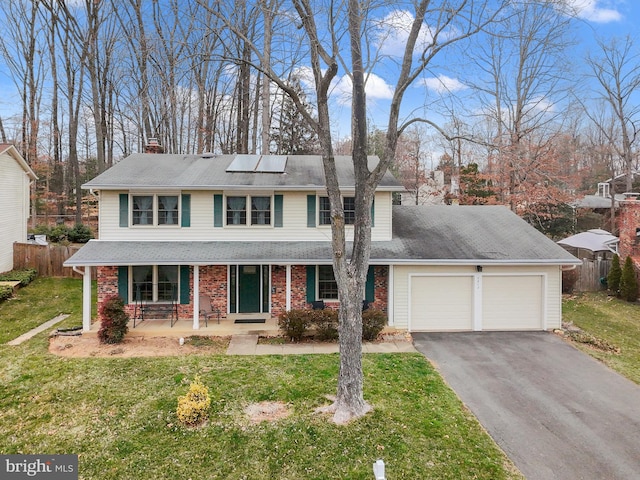 traditional-style house featuring solar panels, a front yard, covered porch, driveway, and an attached garage