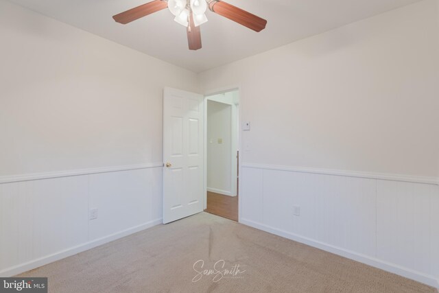 unfurnished room featuring carpet flooring, ceiling fan, and a wainscoted wall