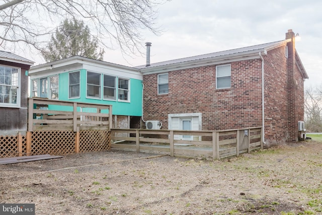 rear view of property featuring metal roof, fence, a wooden deck, a chimney, and brick siding