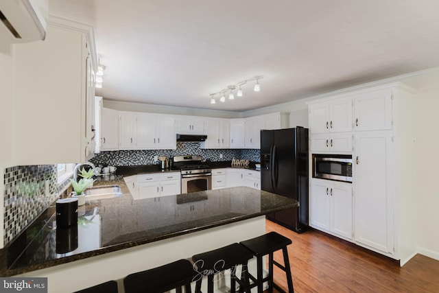 kitchen with decorative backsplash, a peninsula, appliances with stainless steel finishes, under cabinet range hood, and a sink