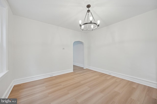 empty room with light wood finished floors, baseboards, arched walkways, and a notable chandelier