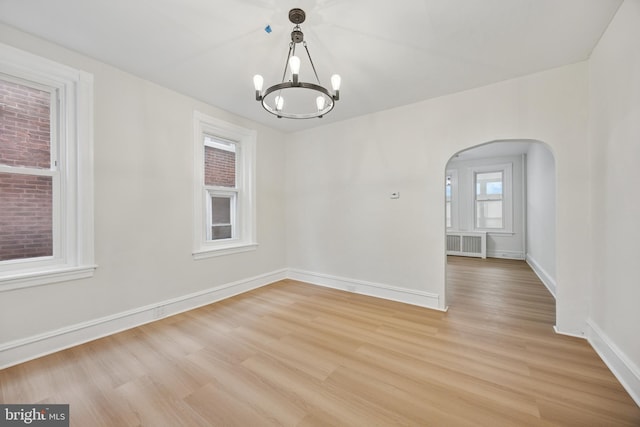 unfurnished room with light wood-style floors, arched walkways, a notable chandelier, and baseboards