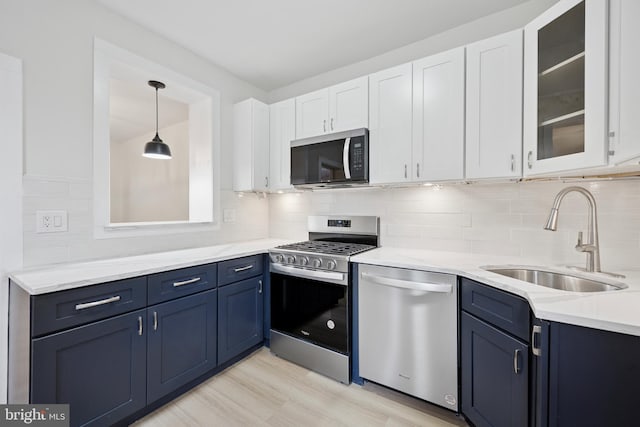 kitchen with stainless steel appliances, a sink, white cabinets, blue cabinetry, and glass insert cabinets