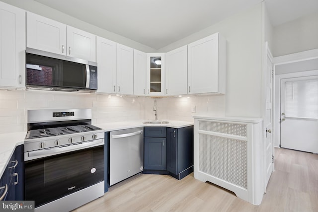 kitchen with appliances with stainless steel finishes, light countertops, light wood-type flooring, white cabinetry, and a sink