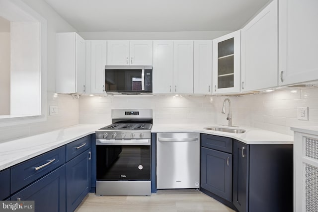 kitchen with blue cabinetry, stainless steel appliances, glass insert cabinets, white cabinets, and a sink