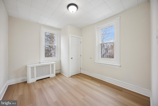 unfurnished bedroom featuring baseboards, multiple windows, wood finished floors, and radiator