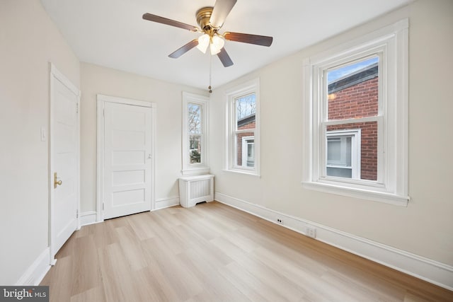 unfurnished bedroom with radiator, light wood-type flooring, baseboards, and a ceiling fan