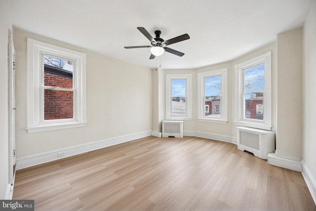 empty room with light wood finished floors, radiator heating unit, and a wealth of natural light